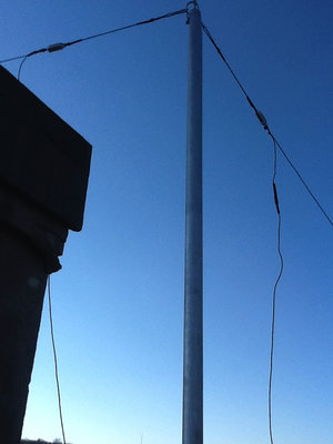 Majd igy nez ki a kifeszites. Nem idealis, mert nem szabadna levezeto huzaloknak lenni a balunhoz, hanem csak megszakitaskent kellett volna a ket antenna vezetek koze tenni a balunt. Sajnos ez csak sokkal maszivabb ruddal lett volna megoldhato, es nagyon szembetuno lett volna a szomszedok reszere. Bele lett kalkulalva az antena hosszba, a kisugarzasi gorbe persze biztosan megsinyli. Az antenna huzal &quot;dx wire&quot; tipus, ami nagyon konnyu, vekonyabb mint 2mm, megis 120kg a szakito szilardsaga, UV vedett a kopenye, uveg szalakkal erositett es joforman nem lathato a magassagban. Hagyomanyos, keskeny porcelan szigeteloket hasznaltam. A rud ezust/szurke szinre festett 3 cm atmerolyu fa, ami igy atfestve nem csak az idojarastol vedett, hanem kevesbe lathato a teton.